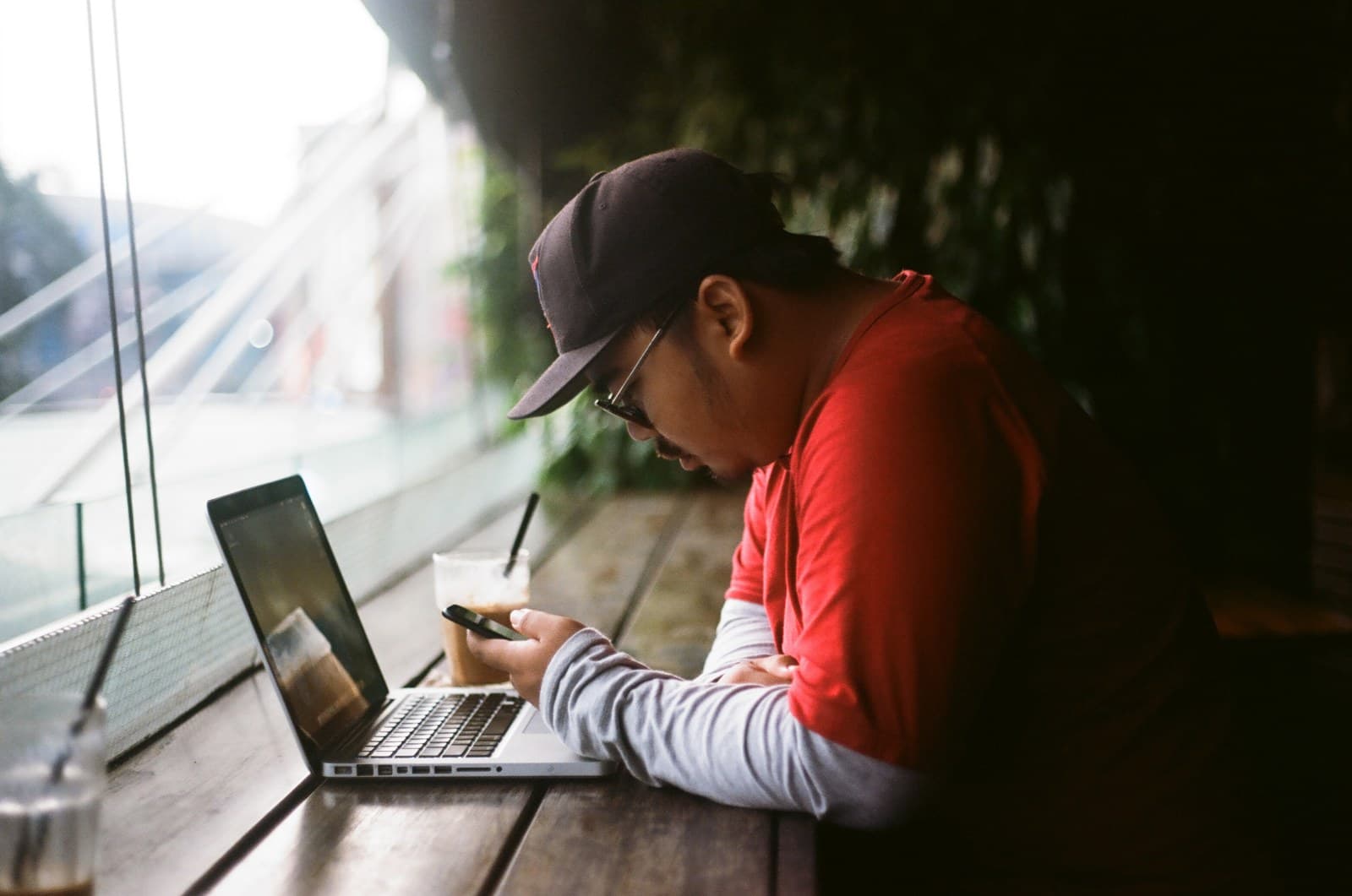 A researcher checking notes on a phone beside an open laptop at a café table.